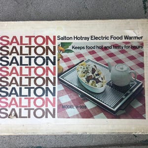 May include: A vintage Salton Hotray Electric Food Warmer box. The box features the brand name in a stacked design with the text "Keeps food hot and tasty for hours." The image shows a food warmer with a plate of food and a teapot on a red and white checkered surface.