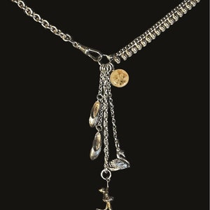May include: Silver necklace with a charm of a ballerina, a swan, and two ballet shoes. The necklace has a silver chain with a small round charm.