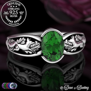 May include: A silver ring with a bright green oval gemstone. The band has a detailed fox and leaf pattern. The ring is hand-crafted and nickel-free. The text "GENUINE STERLING 925 SILVER" is visible.