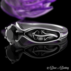 May include: A silver engagement ring with a black diamond and a mushroom design. The ring is set on a black background.