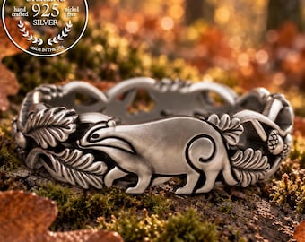 Puede incluir: Un anillo de plata de ley con un diseño en relieve de un tejón rodeado de hojas de roble y bellotas. La banda tiene un acabado mate e incluye un sello circular que dice GENUINE STERLING 925 SILVER hand crafted nickel free MADE IN THE USA.