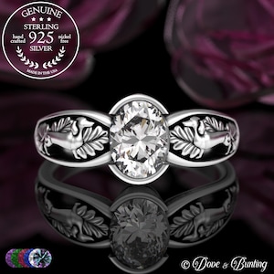 Puede incluir: Un anillo de plata de ley con una gran piedra preciosa transparente de talla ovalada. La banda presenta un diseño de perro salchicha y hojas. El anillo está marcado "Genuine Sterling 925 Silver" y "Made in the USA".