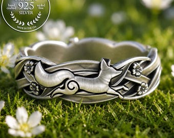 Puede incluir: Un anillo de plata de ley con un motivo de zorro esculpido integrado en una banda con detalles florales. El metal tiene un acabado cepillado. Un sello circular en la esquina superior izquierda dice GENUINE STERLING 925 SILVER hand crafted nickel free.