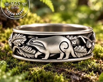 Puede incluir: Un anillo de plata de ley con un diseño en relieve de un tejón caminando entre hojas de roble y bellotas. La banda tiene un acabado mate con detalles oxidados. Un sello circular en la imagen dice Genuine Sterling 925 Silver Hand Crafted.