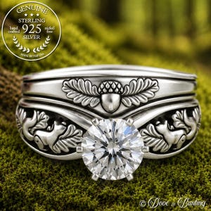 May include: A sterling silver ring featuring a central round faceted stone held by six prongs. The band is decorated with embossed squirrel and oak leaf motifs. A circular seal in the upper left corner reads GENUINE STERLING 925 SILVER.