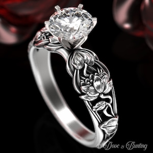Puede incluir: Un anillo de compromiso de plata con un gran diamante redondo y claro y un diseño floral con flores de loto.