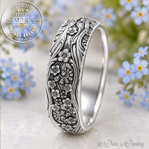 May include: A sterling silver ring featuring a detailed relief pattern of forget-me-not flowers and winding stems. The band has a polished interior and a textured, oxidized exterior finish. A circular seal in the corner reads Genuine Sterling 925 Silver.