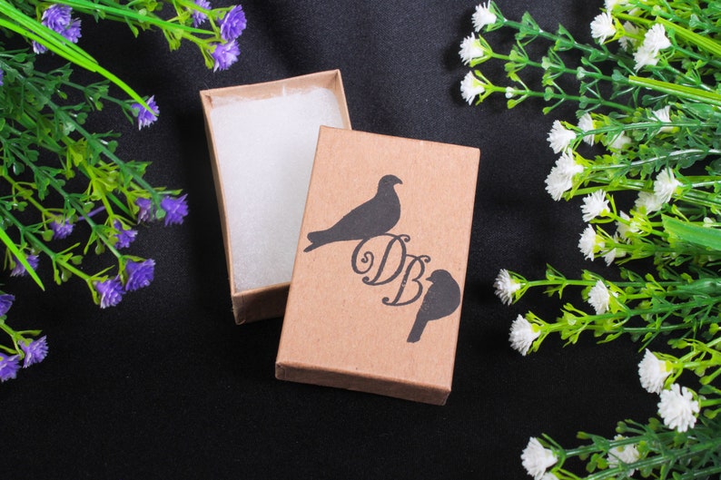 May include: A brown cardboard box with a white interior. The box has a black silhouette of two birds with the initials "DB" printed on the front.