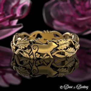 May include: A gold-toned ring with a detailed design of a pig surrounded by leaves and vines. The ring is on a black reflective surface.