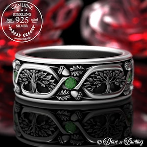 May include: Sterling silver ring with a tree of life design, featuring two intertwined trees with green gemstones and acorn accents. The ring is made in the USA.