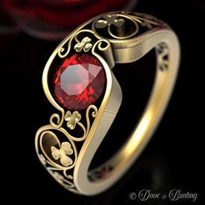 Puede incluir: Un anillo de oro con una piedra preciosa roja engastada en un diseño delicado e intrincado con motivos de trébol. El anillo es una pieza llamativa con un estilo clásico y elegante.