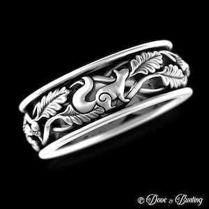 May include: A silver ring with a detailed design of a squirrel, leaves, and acorns. The ring is a wide band with a raised design.