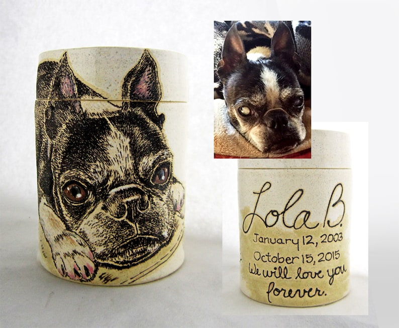 K&ouml;nnte beinhalten: Eine wei&szlig;e Keramikurne mit einer Schwarzwei&szlig;illustration eines Boston Terrier Hundes. Die Urne tr&auml;gt den Text "Lola B" sowie die Daten "12. Januar 2003" und "15. Oktober 2015". Der Text "Wir werden dich f&uuml;r immer lieben." ist ebenfalls auf der Urne geschrieben.
