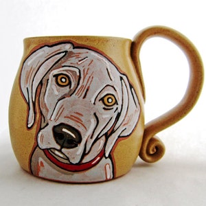 Puede incluir: Una taza de cerámica marrón con una imagen pintada a mano de un perro Weimaraner. El perro lleva un collar rojo y mira directamente al espectador. La taza tiene un asa marrón con un extremo rizado.