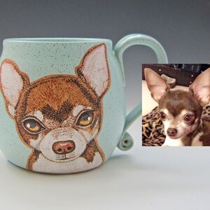 Puede incluir: Una taza de cer&aacute;mica azul claro con una imagen pintada a mano de un chihuahua marr&oacute;n y blanco. La taza tiene un cuerpo redondeado y un asa. Una foto de un chihuahua se muestra en el fondo.