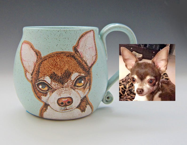 Puede incluir: Una taza de cer&aacute;mica azul claro con una imagen pintada a mano de un chihuahua marr&oacute;n y blanco. La taza tiene un cuerpo redondeado y un asa. Una foto de un chihuahua se muestra en el fondo.