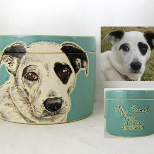 K&ouml;nnte beinhalten: Eine tealfarbene Keramik-Tierurne mit einem handgemalten Portr&auml;t eines schwarz-wei&szlig;en Hundes. Die Urne hat einen Deckel und ist mit "My Sweet Mia 2003-2019" beschriftet.