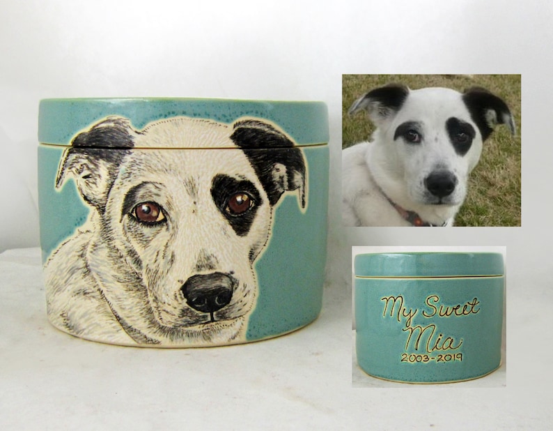 K&ouml;nnte beinhalten: Eine tealfarbene Keramik-Tierurne mit einem handgemalten Portr&auml;t eines schwarz-wei&szlig;en Hundes. Die Urne hat einen Deckel und ist mit "My Sweet Mia 2003-2019" beschriftet.