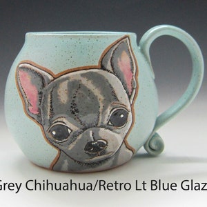 Puede incluir: Una taza de cer&aacute;mica con un esmalte azul claro presenta una ilustraci&oacute;n pintada a mano de un chihuahua gris. La taza tiene un cuerpo redondeado y un asa curva.