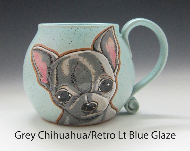 Puede incluir: Una taza de cer&aacute;mica con un esmalte azul claro presenta una ilustraci&oacute;n pintada a mano de un chihuahua gris. La taza tiene un cuerpo redondeado y un asa curva.