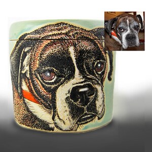 K&ouml;nnte beinhalten: Eine Keramikdose mit einer handgemalten Illustration eines Boxerhundes. Die Dose hat einen hellblauen Hintergrund und der Hund ist in Braun-, Schwarz- und Wei&szlig;t&ouml;nen dargestellt. Der Hund tr&auml;gt ein rotes Halsband.