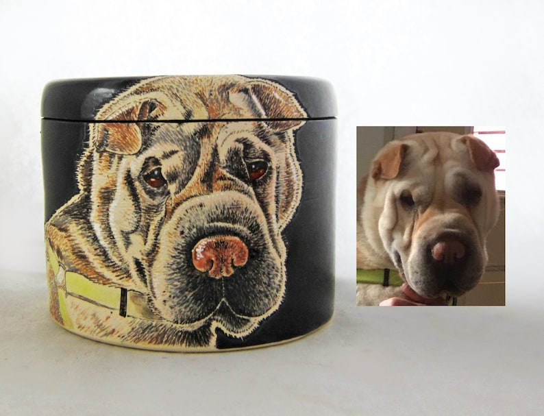 K&ouml;nnte beinhalten: Eine schwarze Keramikdose mit einem handgemalten Bild eines Shar-Pei-Hundes. Der Hund hat ein hellbraunes und schwarzes Fell und schaut direkt auf den Betrachter. Die Dose hat einen Deckel.