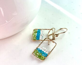 Un arete colgante de forma rectangular en oro de 14k lleno de pepitas de piedras preciosas.