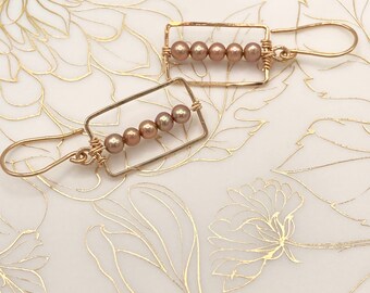 Pendientes colgantes con impresionantes perlas color topo engastadas dentro de un marco de oro hecho a mano.