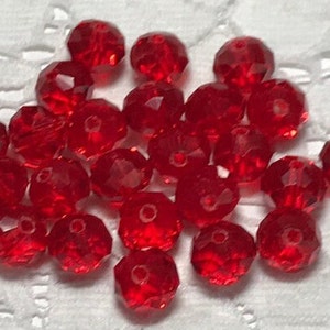 Könnte beinhalten: Eine Sammlung roter facettierter Glasperlen. Die Perlen sind rund und haben eine glänzende Oberfläche.