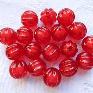 May include: A collection of 18 red glass beads with a ribbed texture. The beads are round and have a glossy finish.