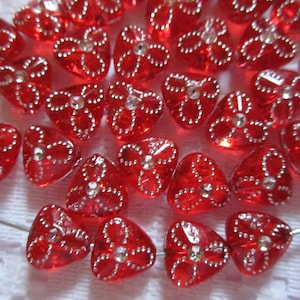 May include: A collection of red glass heart-shaped beads with silver glitter accents. The beads are strung on a silver wire.