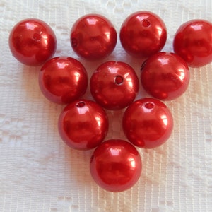 Könnte beinhalten: Zehn rote Perlen, jede mit einer glatten, glänzenden Oberfläche. Die Perlen sind in einem dreieckigen Muster auf einer weißen Oberfläche angeordnet.