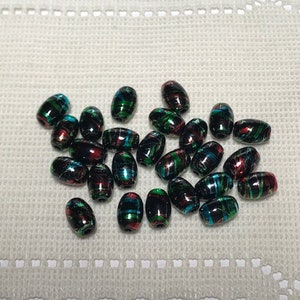 May include: A collection of oval-shaped beads with a black base and a colorful pattern of green, red, and blue. The beads are scattered on a white surface.