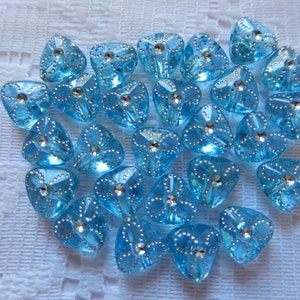 May include: A collection of 25 light blue, triangular-shaped buttons with silver accents. The buttons have a shiny, iridescent finish.