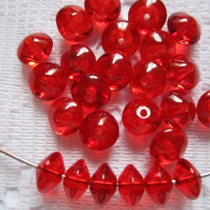 May include: A collection of red glass beads, some are round and some are faceted. The beads are arranged in a pile and on a silver wire.