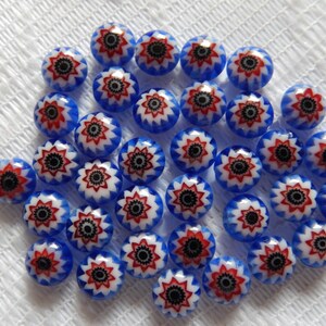 Puede incluir: Una colección de 25 cuentas de vidrio azul con un patrón de estrella blanca y roja. Las cuentas son redondas y tienen un acabado brillante.