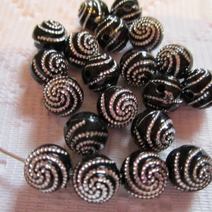 May include: A collection of black and silver beads with a spiral design. The beads are round and have a shiny finish.