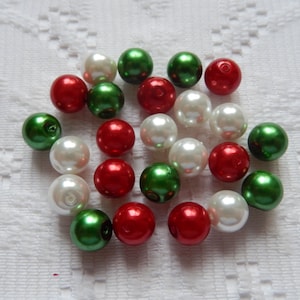 May include: A collection of round, white, red, and green beads. The beads are arranged in a loose circle on a white surface.