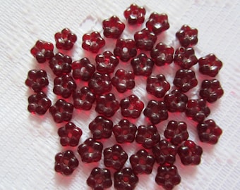 May include: A pile of small, red, glass flower-shaped beads. The beads have a hole in the center for stringing.