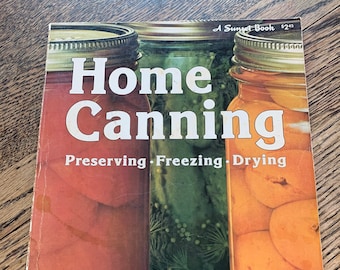 May include: A vintage cookbook titled "Home Canning" with the subtitle "Preserving, Freezing, Drying." The cover features images of preserved foods in glass jars. The book is a Sunset Book.