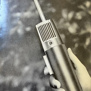 May include: A vintage Toshiba Columnar Type Transceiver advertisement featuring a black and white image of a handheld radio device with a long antenna, a speaker grille, and a side button, set against a dark, out-of-focus background.