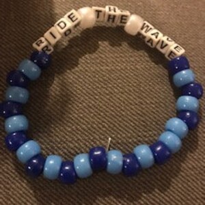 May include: Blue and white beaded bracelet with the words "Ride the Wave" spelled out in white beads.