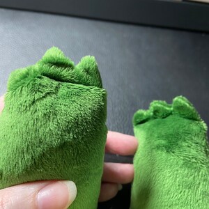Op de afbeelding: Close-up van twee groene pluche voeten met een textuur. De voeten zijn aan de bovenkant aan elkaar genaaid.