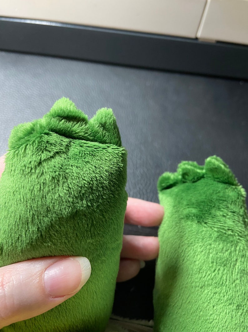 Op de afbeelding: Close-up van twee groene pluche voeten met een textuur. De voeten zijn aan de bovenkant aan elkaar genaaid.
