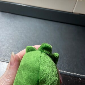 Op de afbeelding: Groen pluche speelgoed met een textuur en een klein, puntig hoofd. Het speelgoed is gevormd als een dinosaurus.