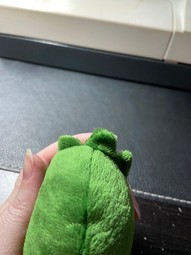 Op de afbeelding: Groen pluche speelgoed met een textuur en een klein, puntig hoofd. Het speelgoed is gevormd als een dinosaurus.