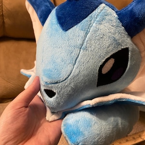 Puede incluir: Un juguete de peluche azul y blanco con una cabeza grande y un cuerpo peque&ntilde;o. El juguete tiene un cuello blanco y una cara azul con ojos negros.