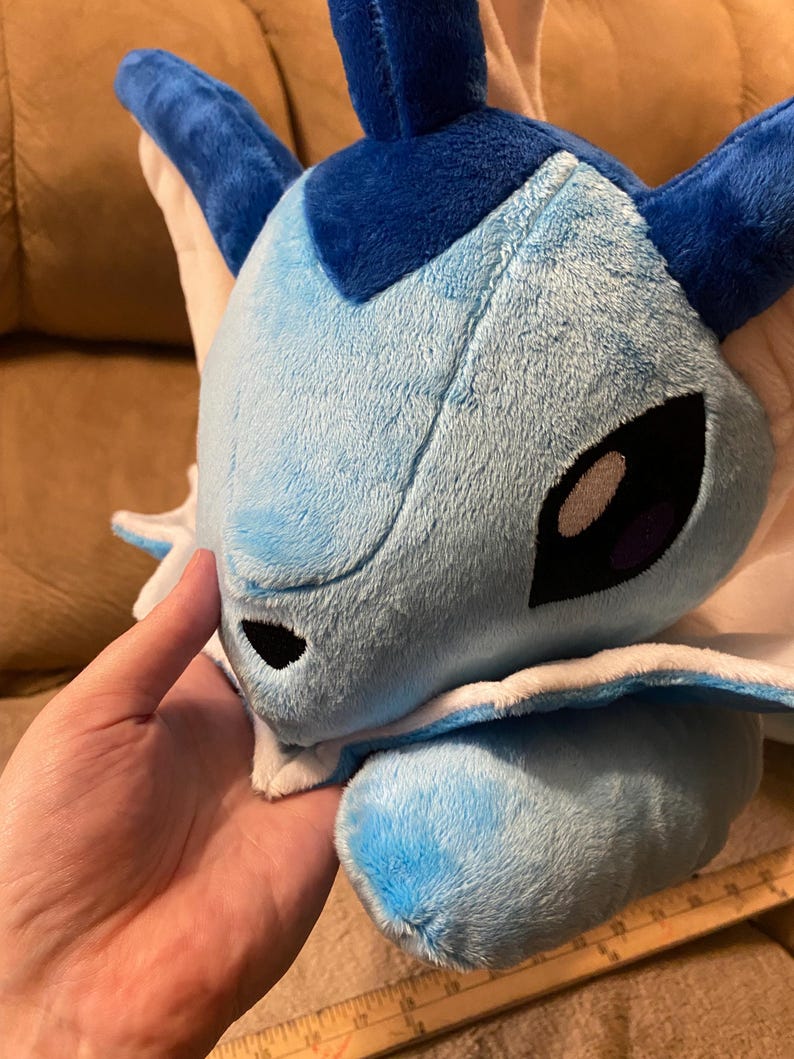 Puede incluir: Un juguete de peluche azul y blanco con una cabeza grande y un cuerpo peque&ntilde;o. El juguete tiene un cuello blanco y una cara azul con ojos negros.