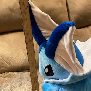 Puede incluir: Un juguete de peluche azul y blanco con forma de personaje Pokemon. El juguete mide aproximadamente 40 cm de alto y est&aacute; sentado en un sof&aacute; marr&oacute;n.
