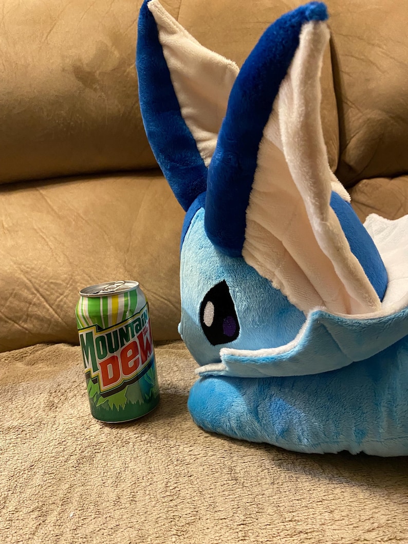 Puede incluir: Un juguete de peluche azul y blanco con orejas grandes, que se asemeja a un personaje de dibujos animados, est&aacute; acostado en un sof&aacute; marr&oacute;n junto a una lata de Mountain Dew.